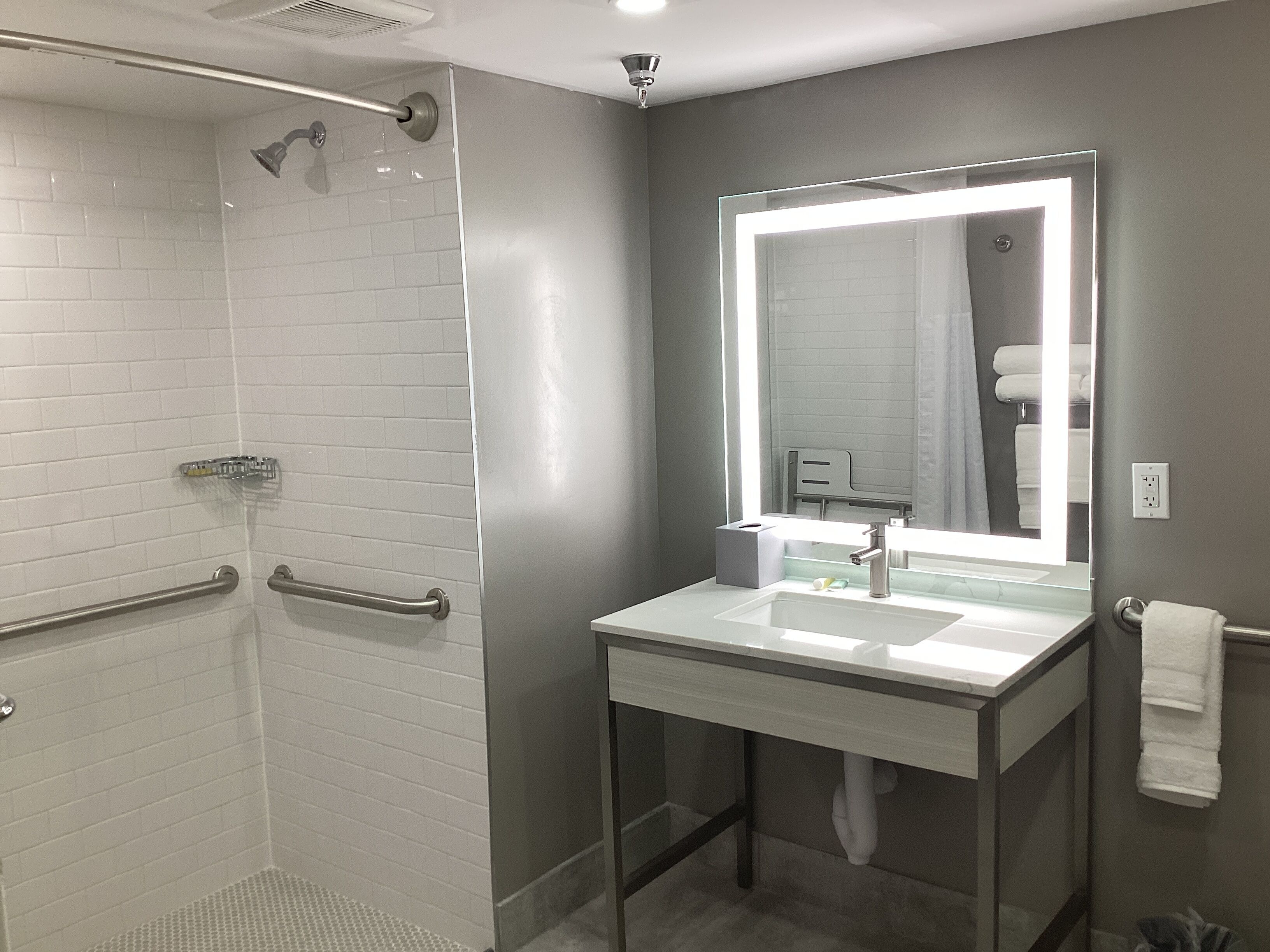 Un baño moderno con ducha a ras de suelo, lavamanos con cerramiento de vidrio y un espejo grande.