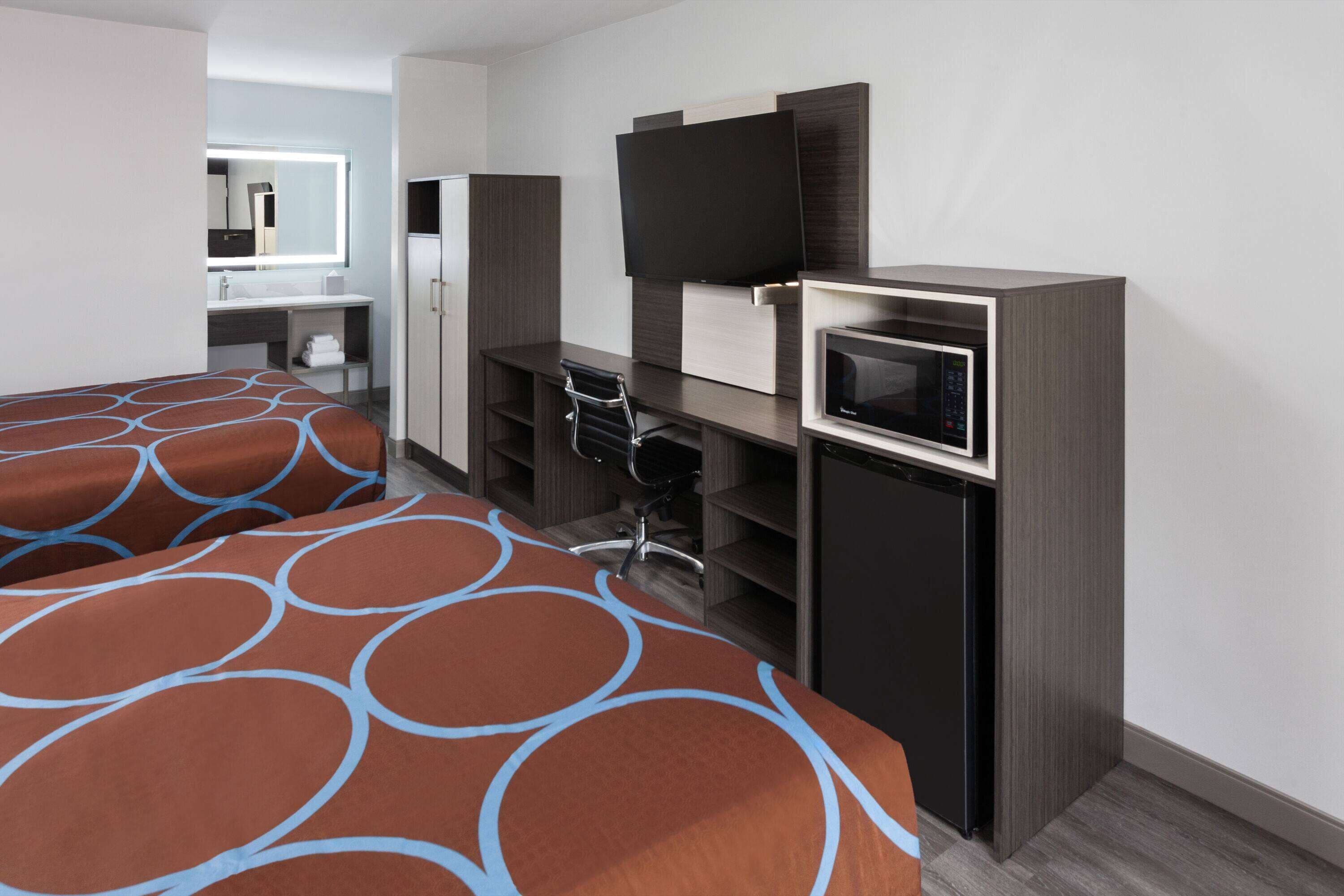 Habitación de hotel con dos camas, un escritorio, un televisor de pantalla plana, un microondas y una kitchenette pequeña.