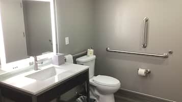 A modern bathroom with a vanity, toilet, and handrail.