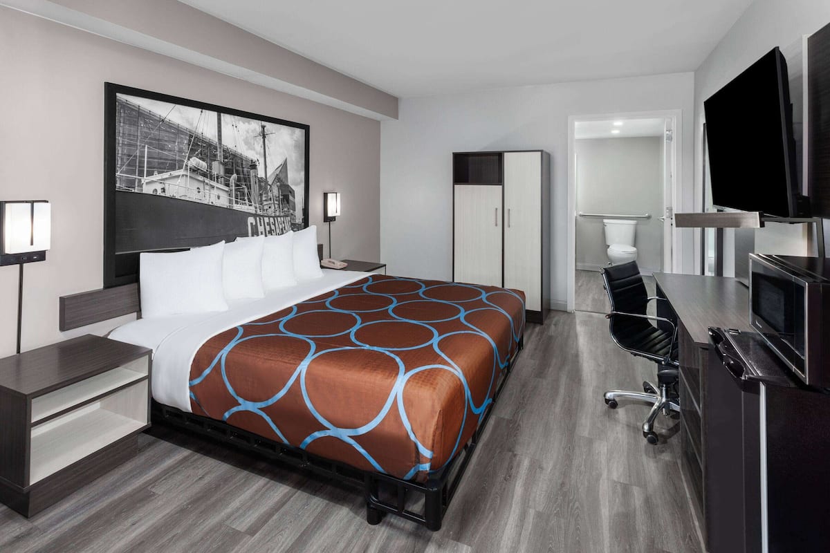 Moderni hotellihuone, jossa on suuri sänky, työpöytä, televisio ja vaatekaappi.