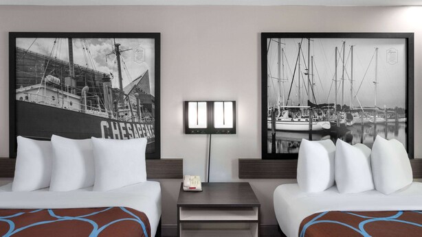 A hotel room with two beds, a nightstand with a phone, and two framed black and white maritime photographs on the wall. - Super 8 By Wyndham Baltimore Northwest (Baltimore)