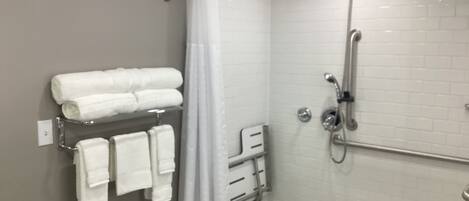 A modern shower area with a glass door, a towel rack with neatly folded towels, and a handheld showerhead.