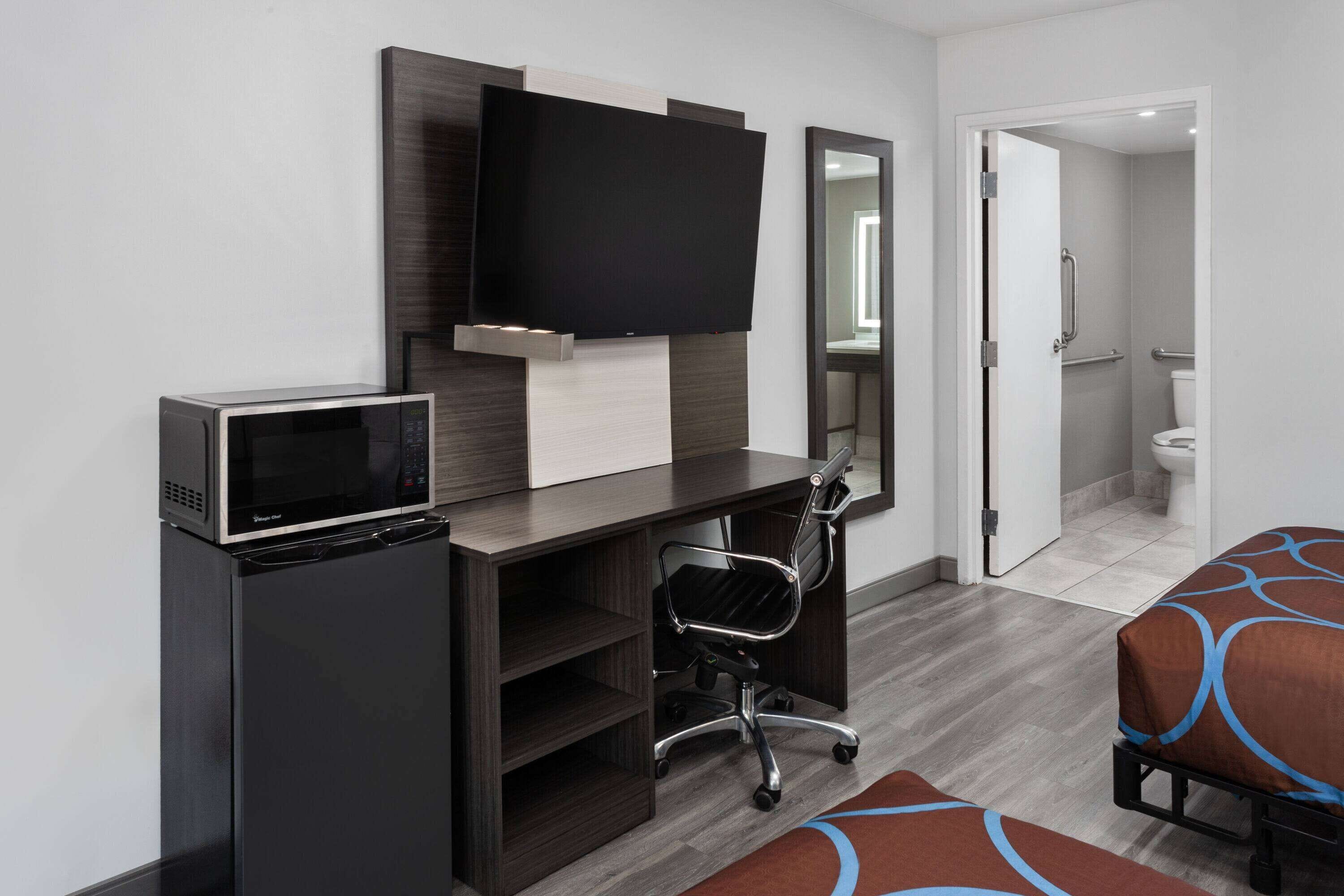 Une chambre d’hôtel équipée d’un bureau, d’une télévision à écran plat, d’un four à micro-ondes, d’une chaise et d’un lit.
