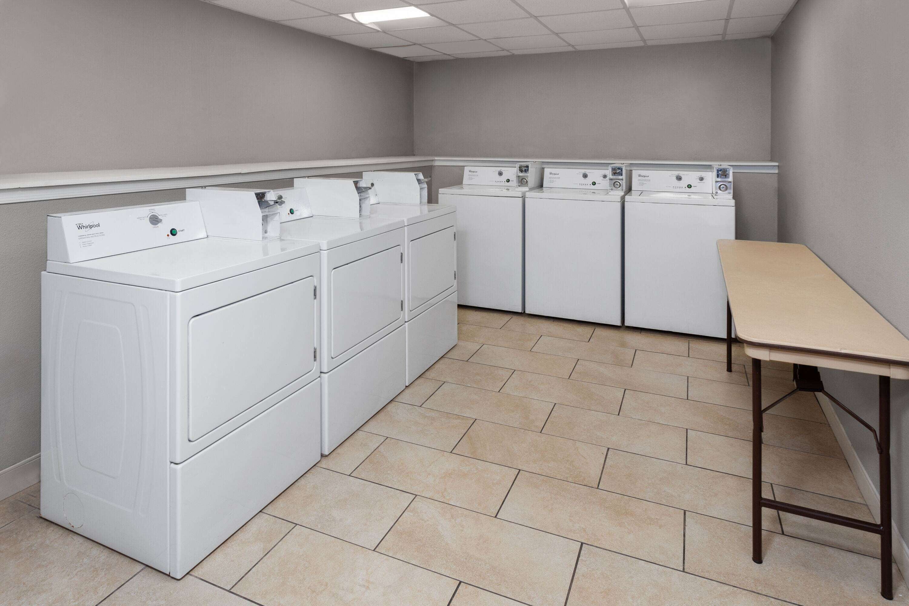 A laundry room with stacked washers and dryers, a table, and tiled flooring.