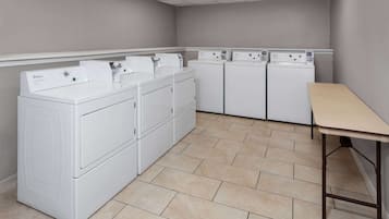 A laundry room with stacked washers and dryers, a table, and tiled flooring.