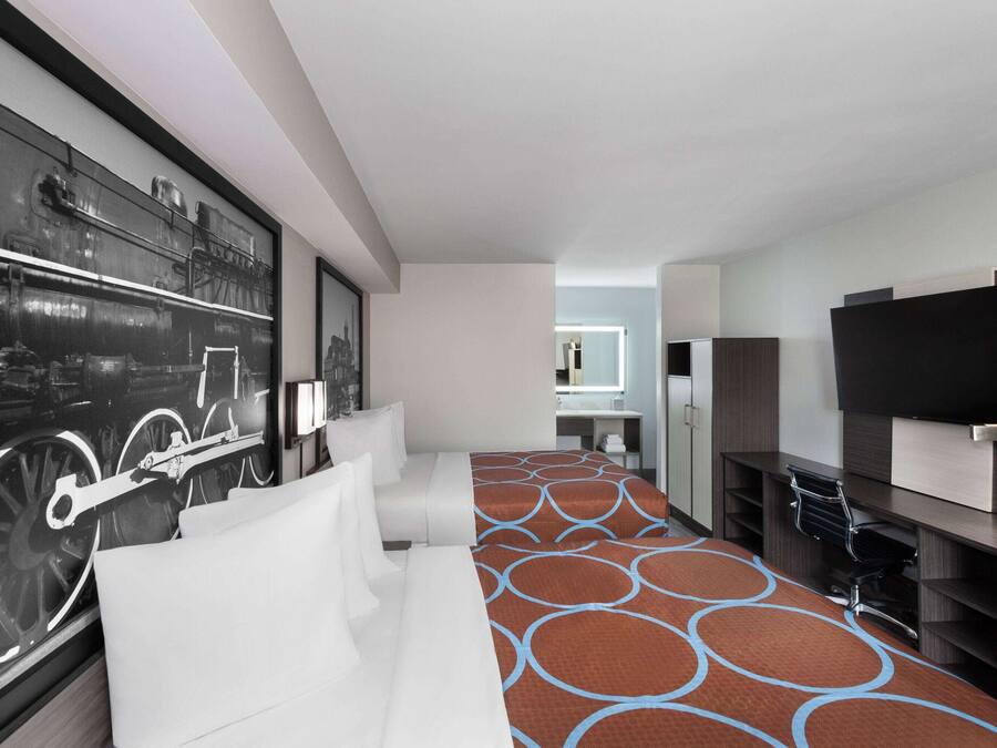 Una habitación de hotel moderna con una cama grande, un escritorio, un televisor y una obra de arte colgada en la pared.