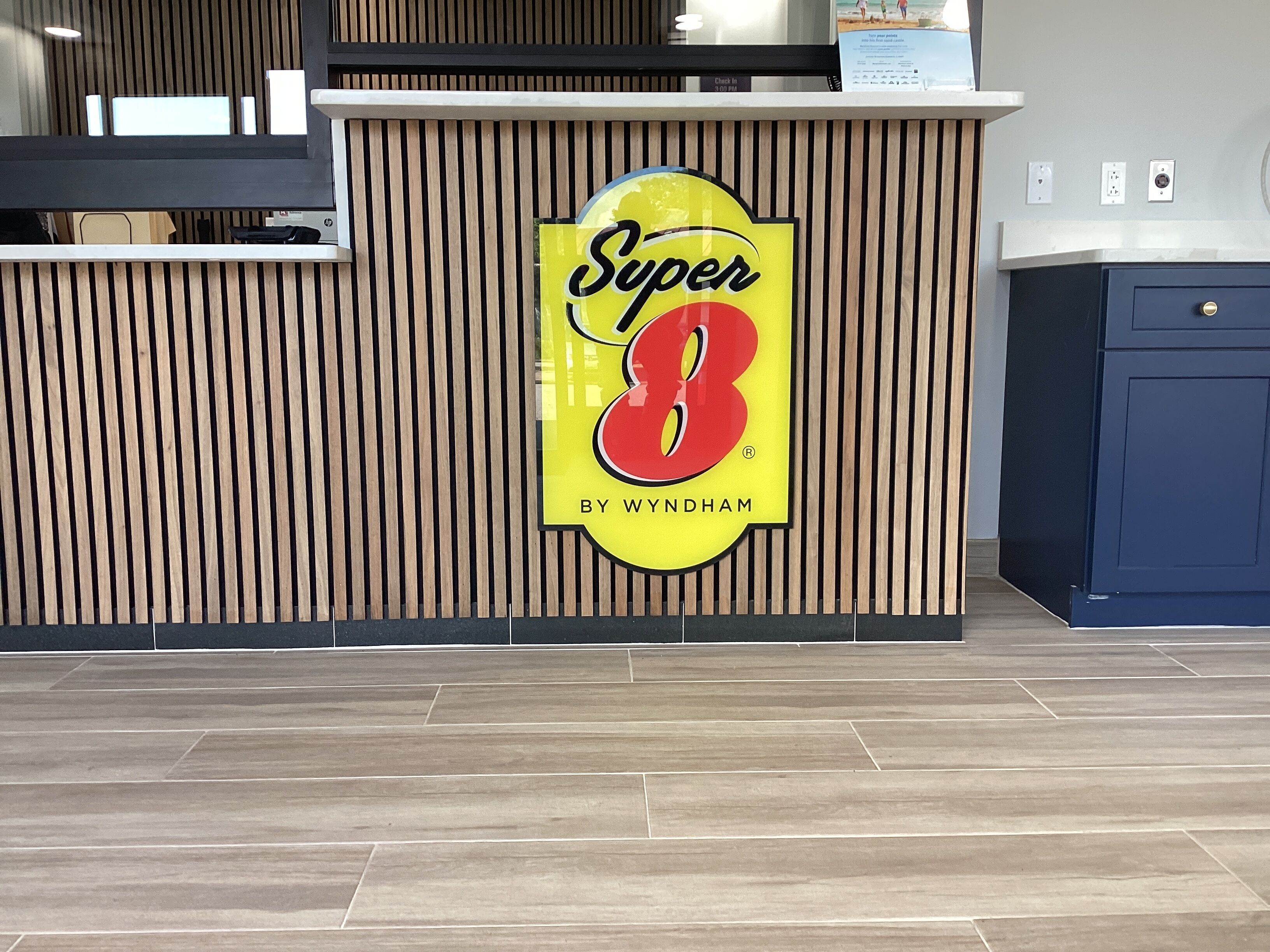 A reception desk with a logo that reads "Super 8 by Wyndham" on a wooden panel wall.