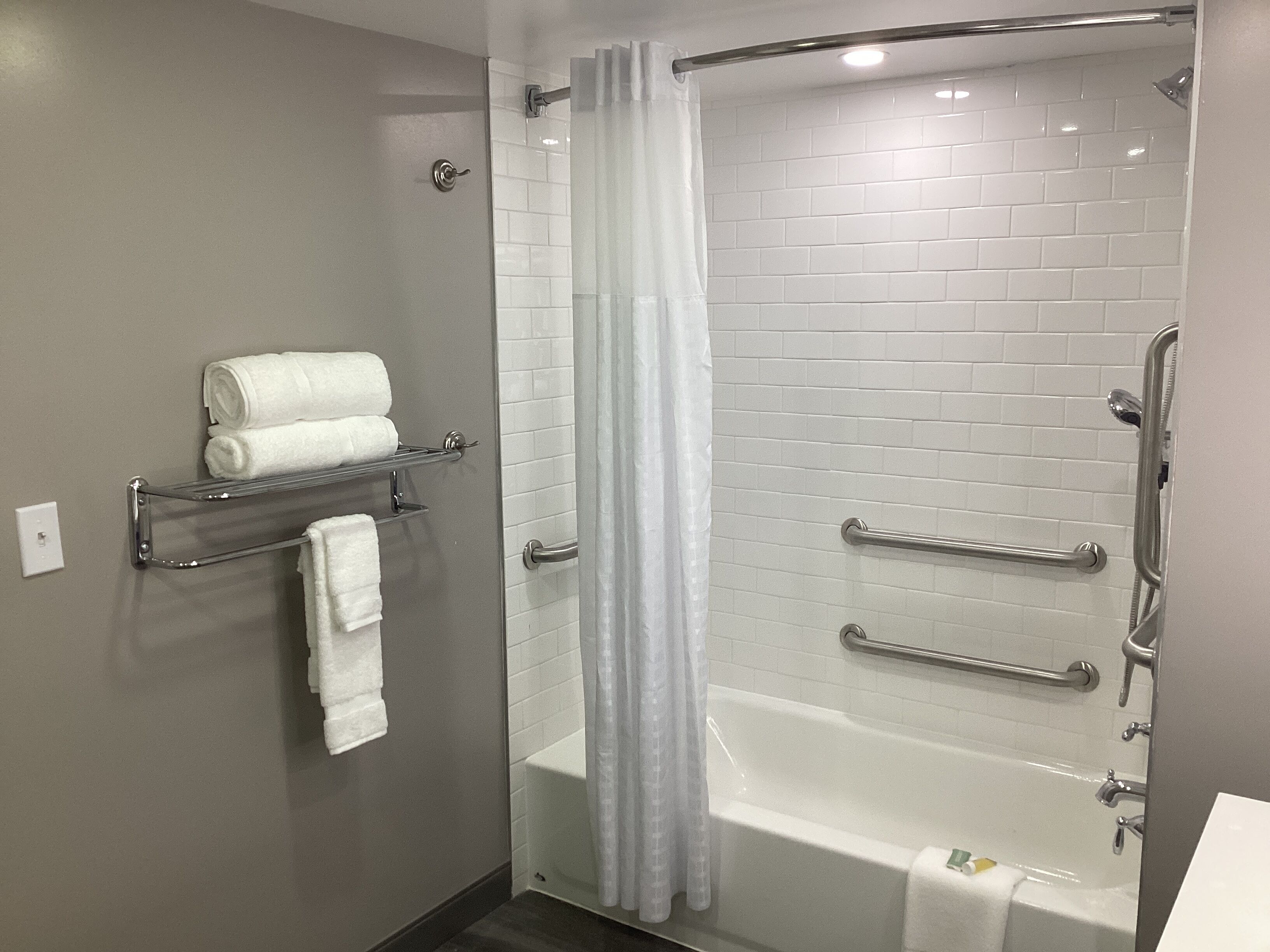 Ein modernes Badezimmer mit einer begehbaren Dusche, einer Badewanne und einem Handtuchhalter mit gefalteten Handtüchern.