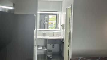 Habitación de hotel pequeña y funcional con kitchenette, baño reducido, ventana con vistas y una cama.