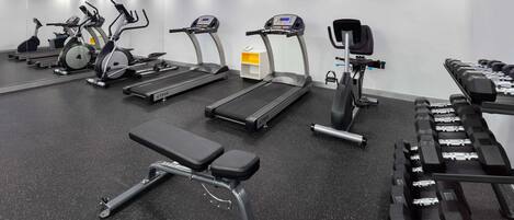 A gym with treadmills, elliptical machines, a bench, and a rack of dumbbells.