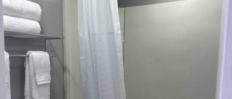 Une salle de bain comprenant des toilettes, une douche avec un rideau et un porte-serviettes avec des serviettes pliées.
