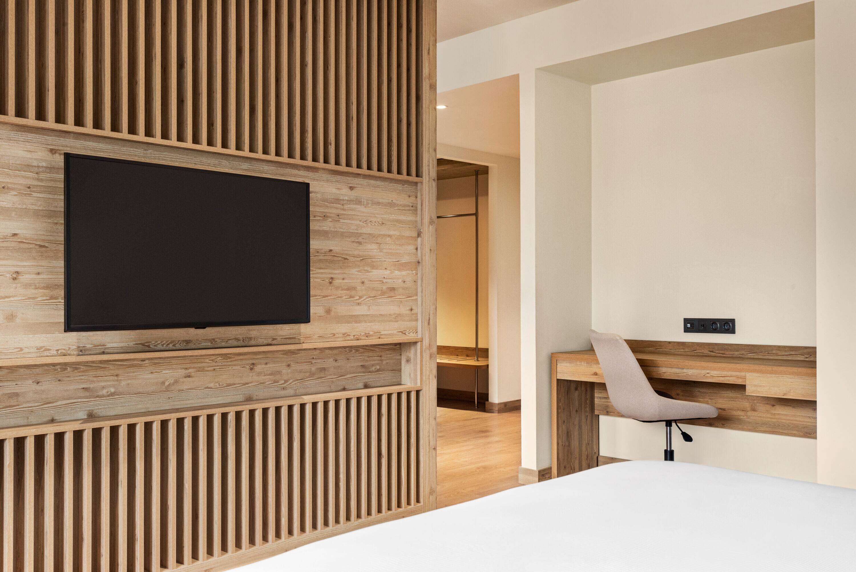 Une chambre d’hôtel moderne avec un mur d’accent en bois, un téléviseur à écran plat, un bureau avec une chaise et une table de chevet.