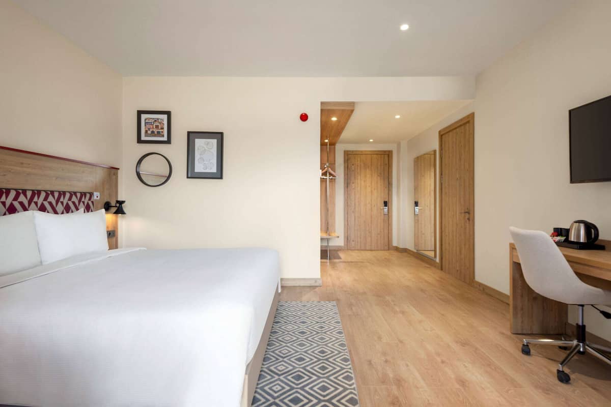 Une chambre d’hôtel avec un grand lit, un bureau avec une chaise, un miroir et des tableaux encadrés accrochés au mur.