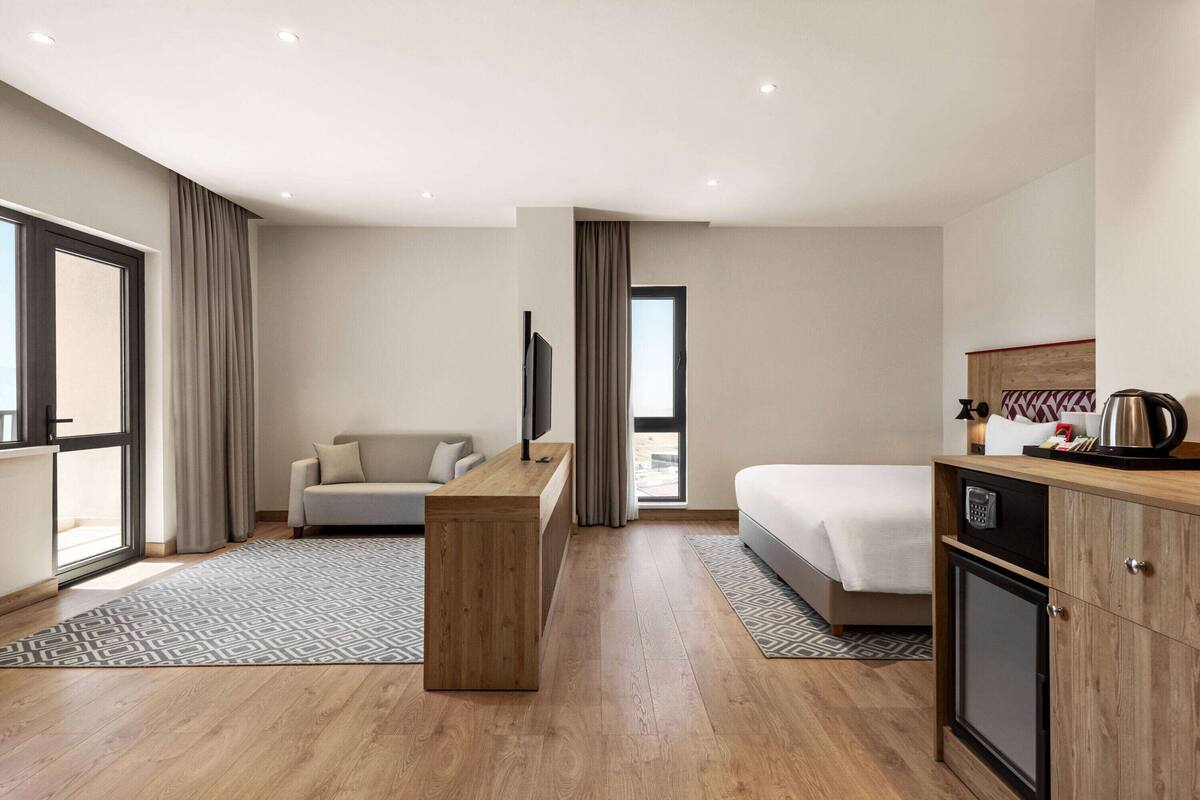 Une chambre d’hôtel moderne équipée d’un bureau en bois, d’un canapé, d’un lit et d’une kitchenette.