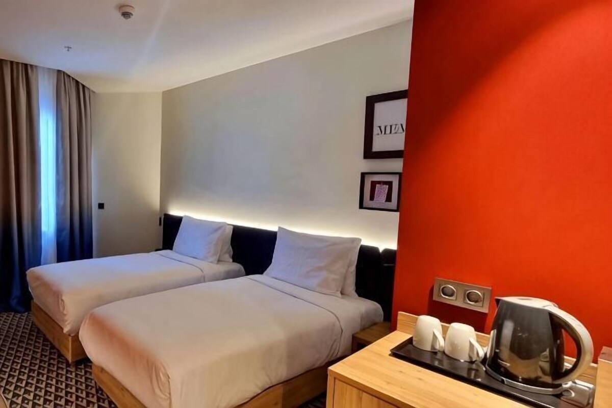 Hotellihuone, jossa on kaksi sänkyä, puinen yöpöytä, jossa on vedenkeitin, ja yksi seinä on maalattu punaisella korostevärillä.