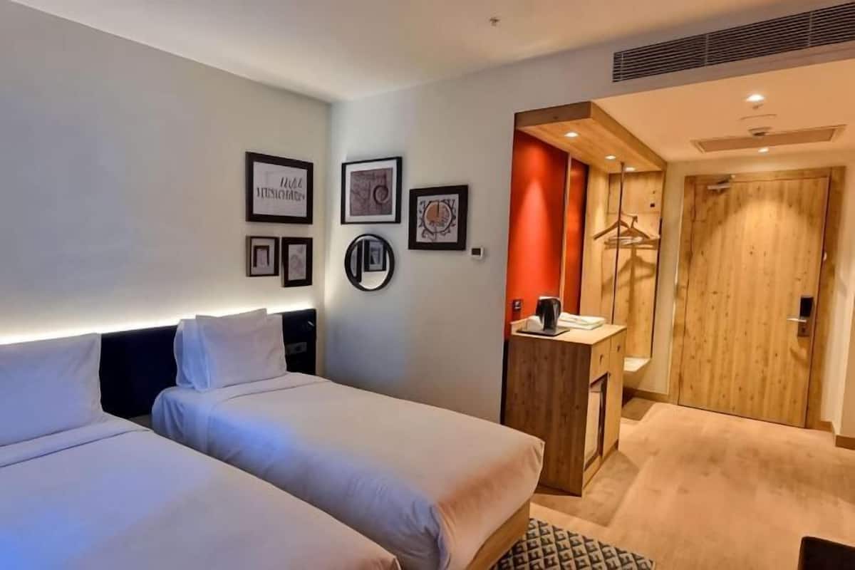 Ein Hotelzimmer mit zwei Betten, einem Schreibtisch mit Stuhl, einem Spiegel und einem Kleiderschrank.