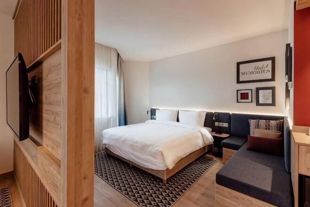 Ein Hotelzimmer mit einem Bett, Nachttischen, einem Fernseher und einem an der Wand befestigten Kunstwerk.