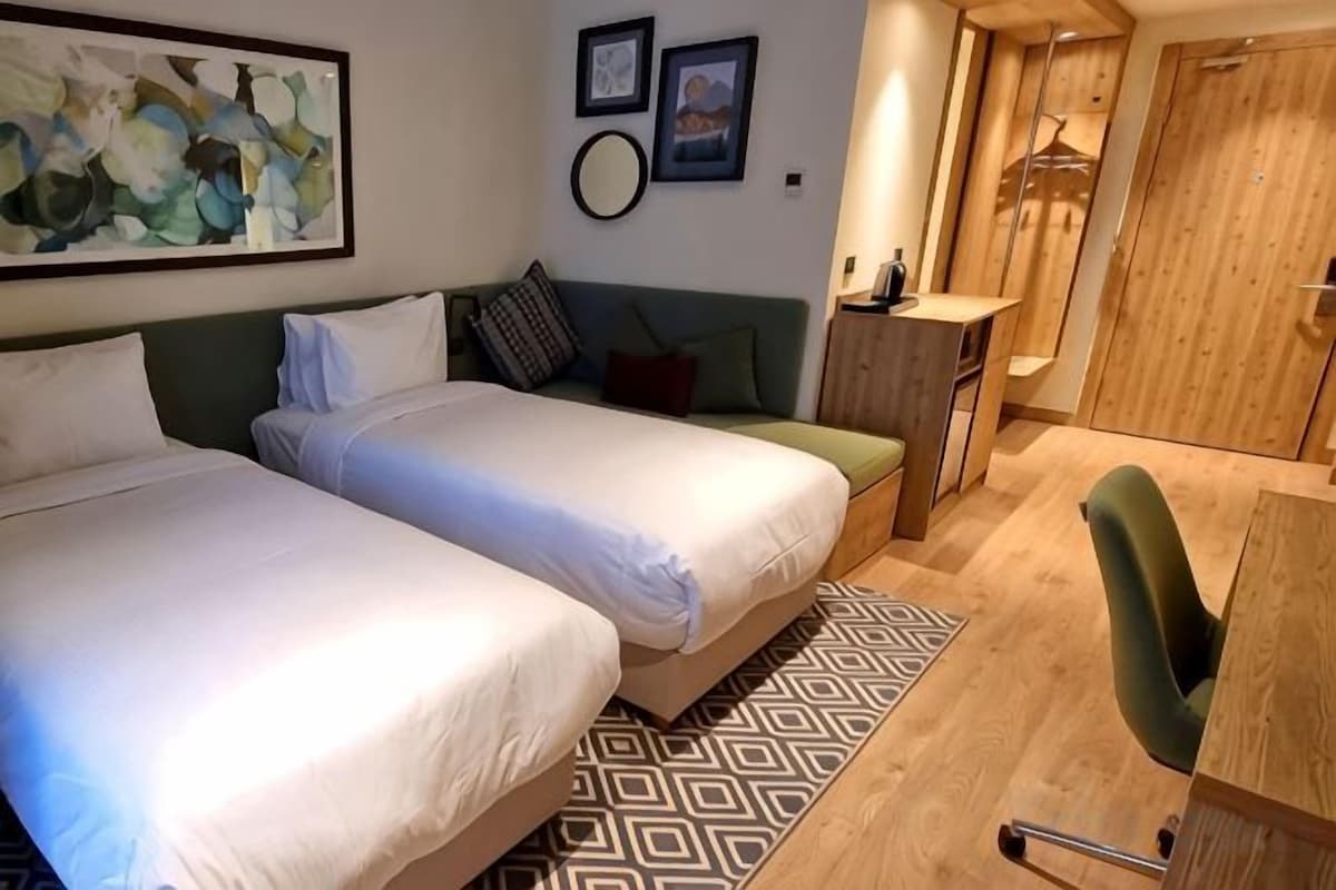 Une chambre d’hôtel avec deux lits, un bureau, une chaise et une armoire.