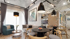 Una sala de estar moderna con un sofá, mesas redondas y sillas. Hay obras de arte en las paredes y un gran ventanal con cortinas.