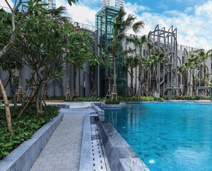 A swimming pool with a modern design, surrounded by palm trees and a building with a glass facade.
