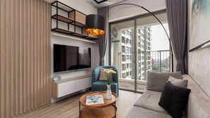 Una sala moderna con un televisor de pantalla plana, un sillón azul, una mesa de centro redonda de madera y un sofá gris.