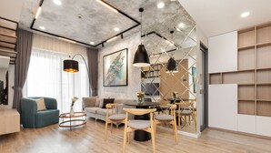 Una sala moderna con un sofá, sillones, una mesa de centro y una zona de comedor con mesa y sillas. Se aprecia una estantería y un cuadro en la pared.
