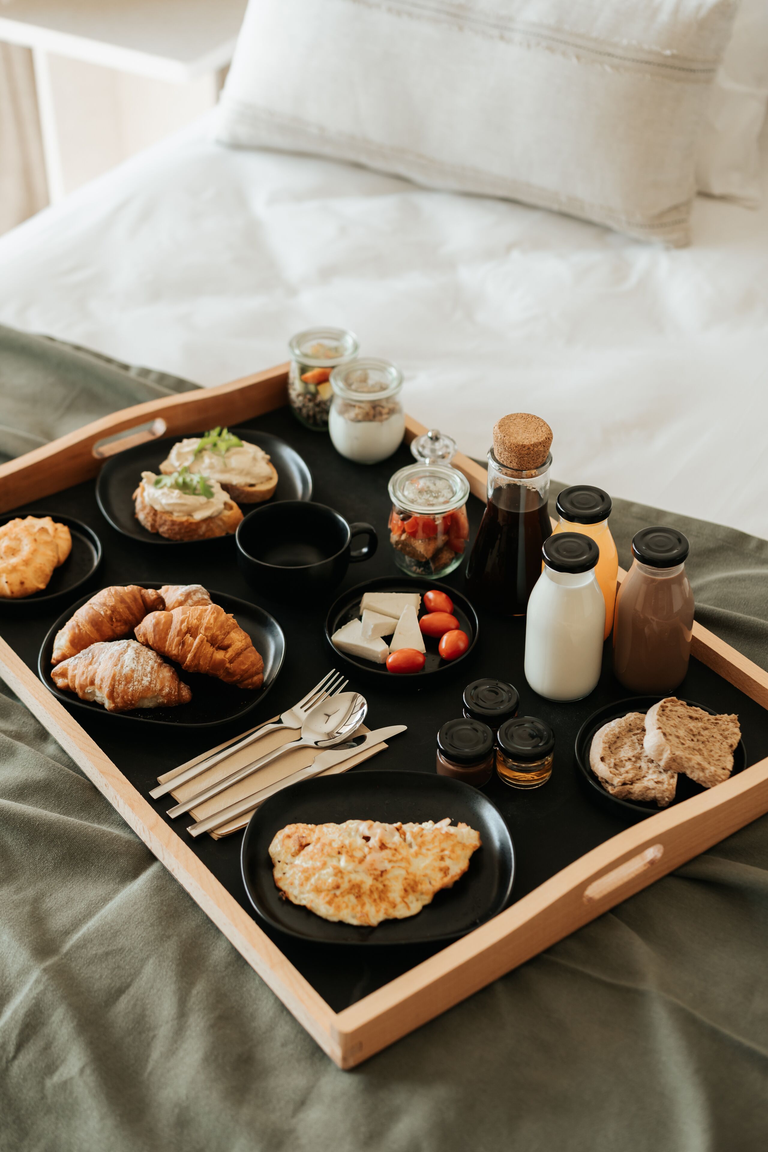 Bandeja de café da manhã com croissants, queijo, tomates e bebidas sobre a cama.
