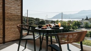 A balcony with a table set for breakfast, wicker chairs, and a view of a mountainous landscape. - AMÉNTE Mindful Stay (Agios Vasileios)