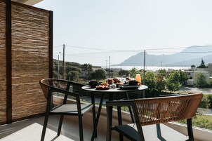 Un balcon avec une table préparée pour le petit-déjeuner, des chaises en osier et une vue sur un paysage montagneux.
