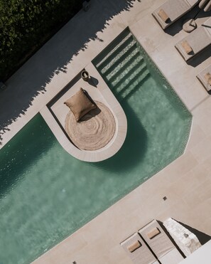Vista aérea de una zona de piscina con un espacio de estar circular, sillas de descanso y un muro de piedra.