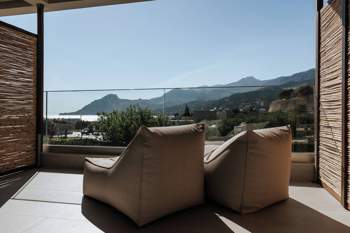 A balcony with two cushioned chairs, a view of a mountainous landscape, and a wooden slatted wall.