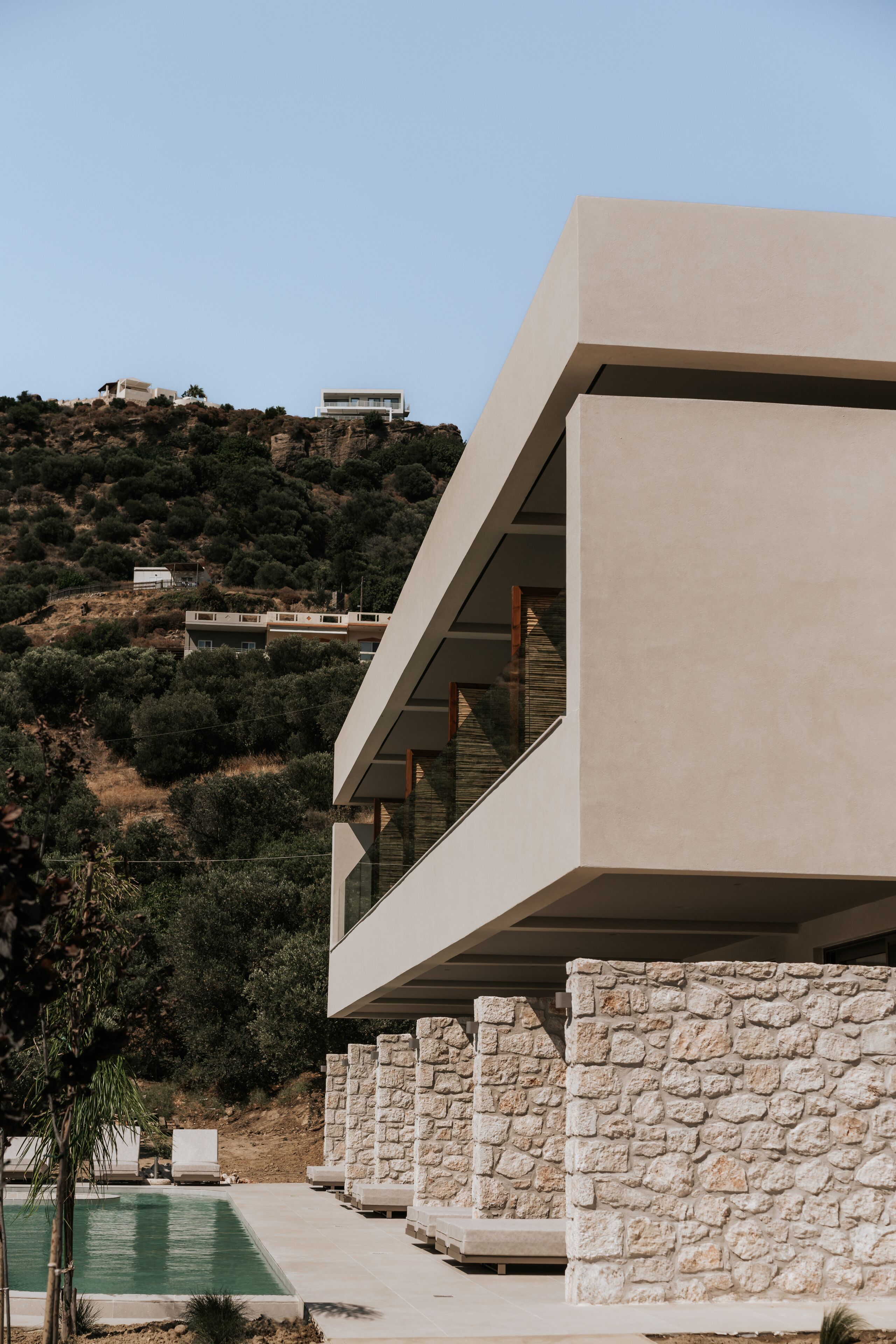 A modern building with a pool, stone walls, and a hillside view.