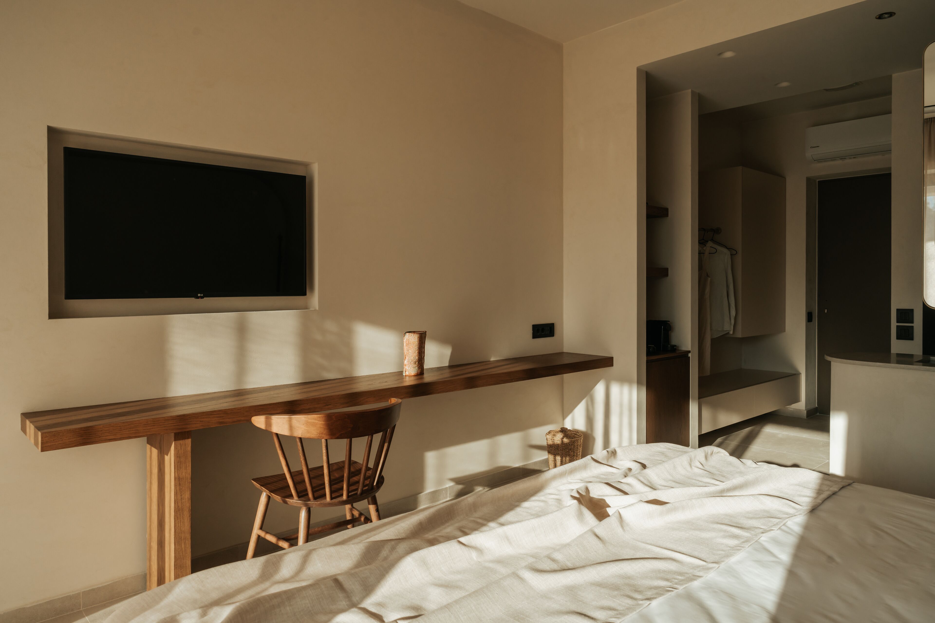A bedroom with a bed, a desk, and a chair. There is a TV mounted on the wall.