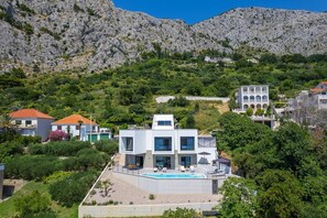 Une villa moderne dotée d’une piscine, entourée d’une végétation luxuriante et de collines rocheuses.