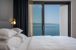 Une chambre d’hôtel avec un grand lit, une tête de lit dotée d’un luminaire et une vue sur la mer, accessible par une porte-fenêtre coulissante.