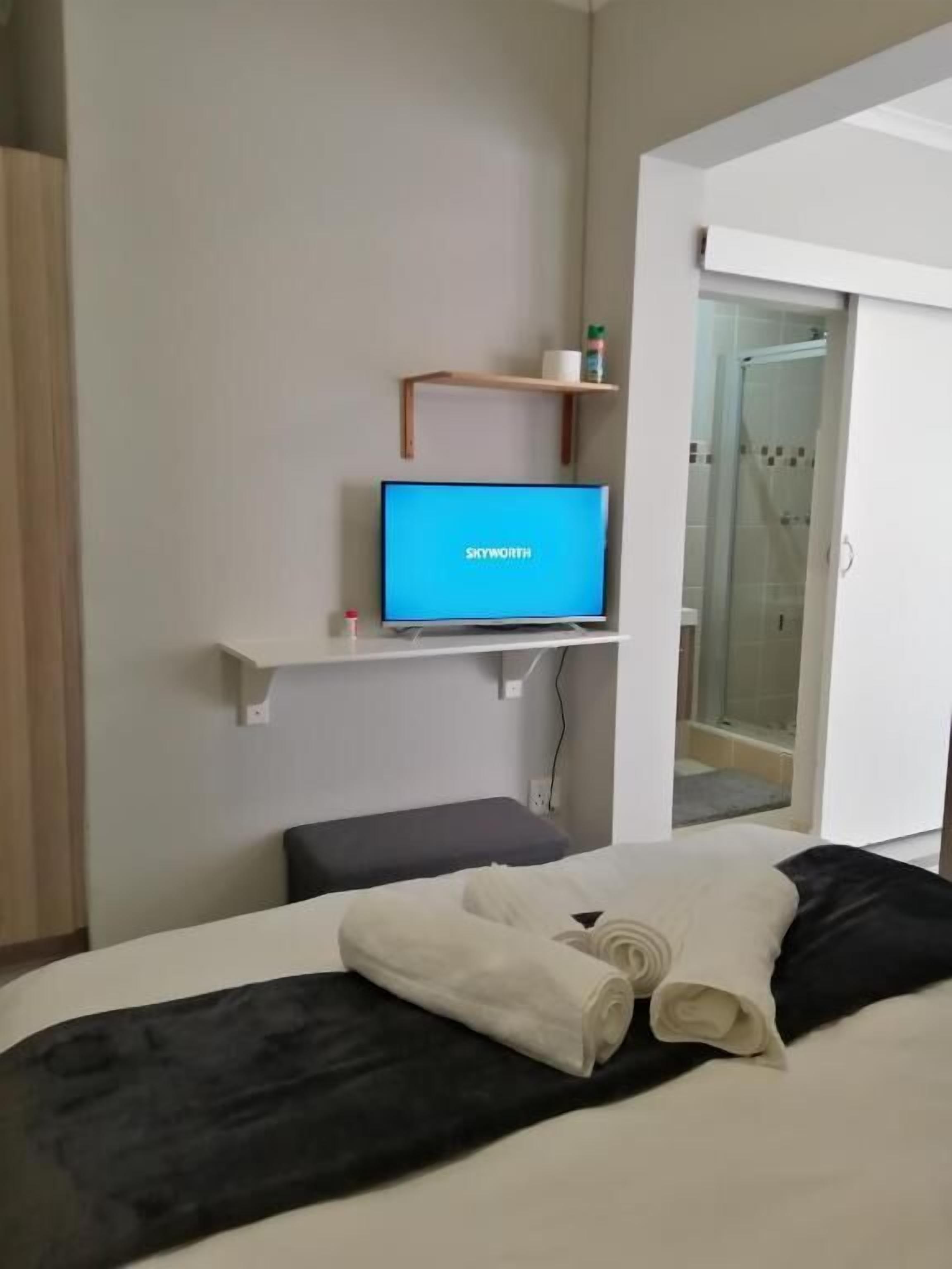 Quarto de hotel com uma cama, televisão em uma estante, área de chuveiro e um pequeno banco.