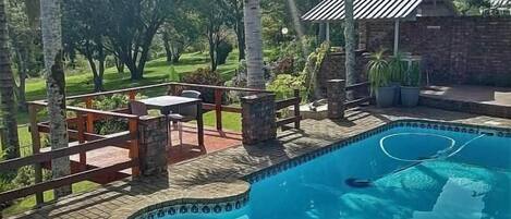 A swimming pool with a brick deck, surrounded by palm trees and a stone wall.