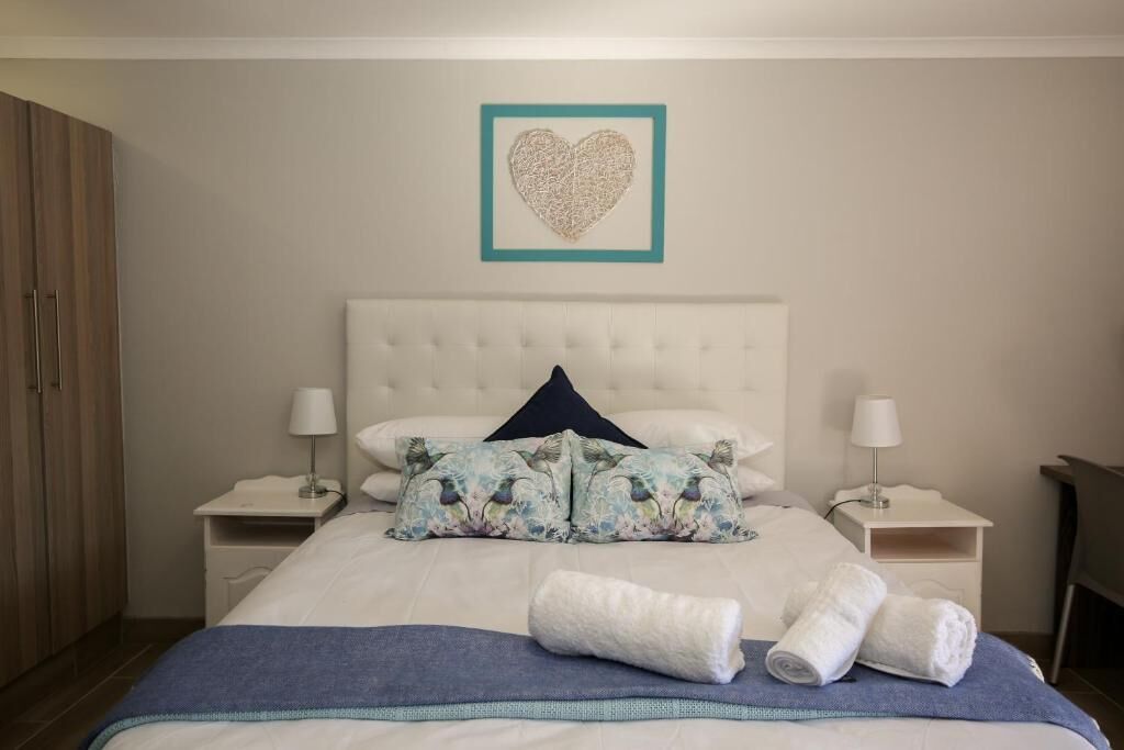 Een keurig opgemaakt hotelkamer met een groot bed, twee nachtkastjes met lampen, een garderobe en een decoratieve hartvormige afbeelding aan de muur.