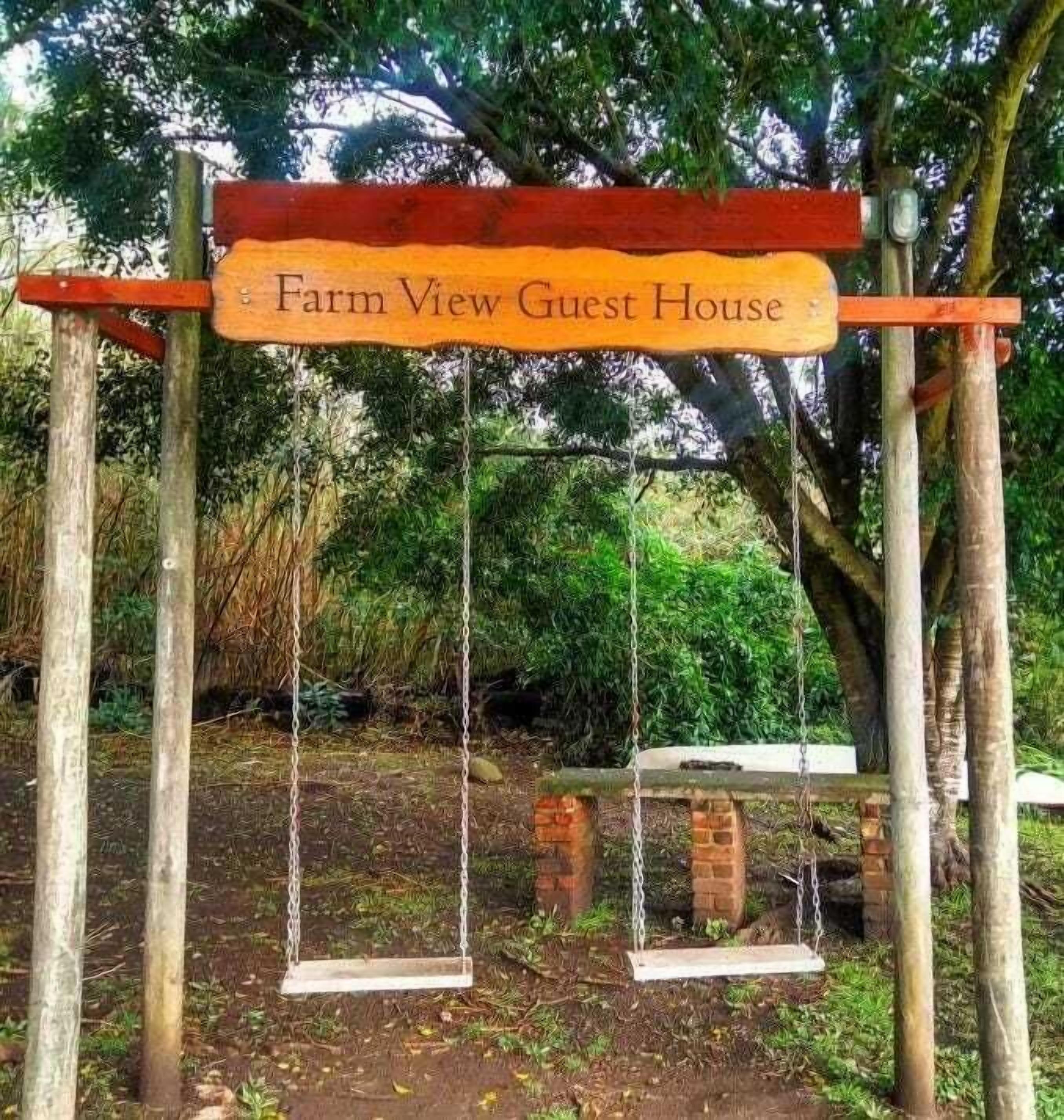 A wooden sign for Farm View Guest House with a swing set in the background.