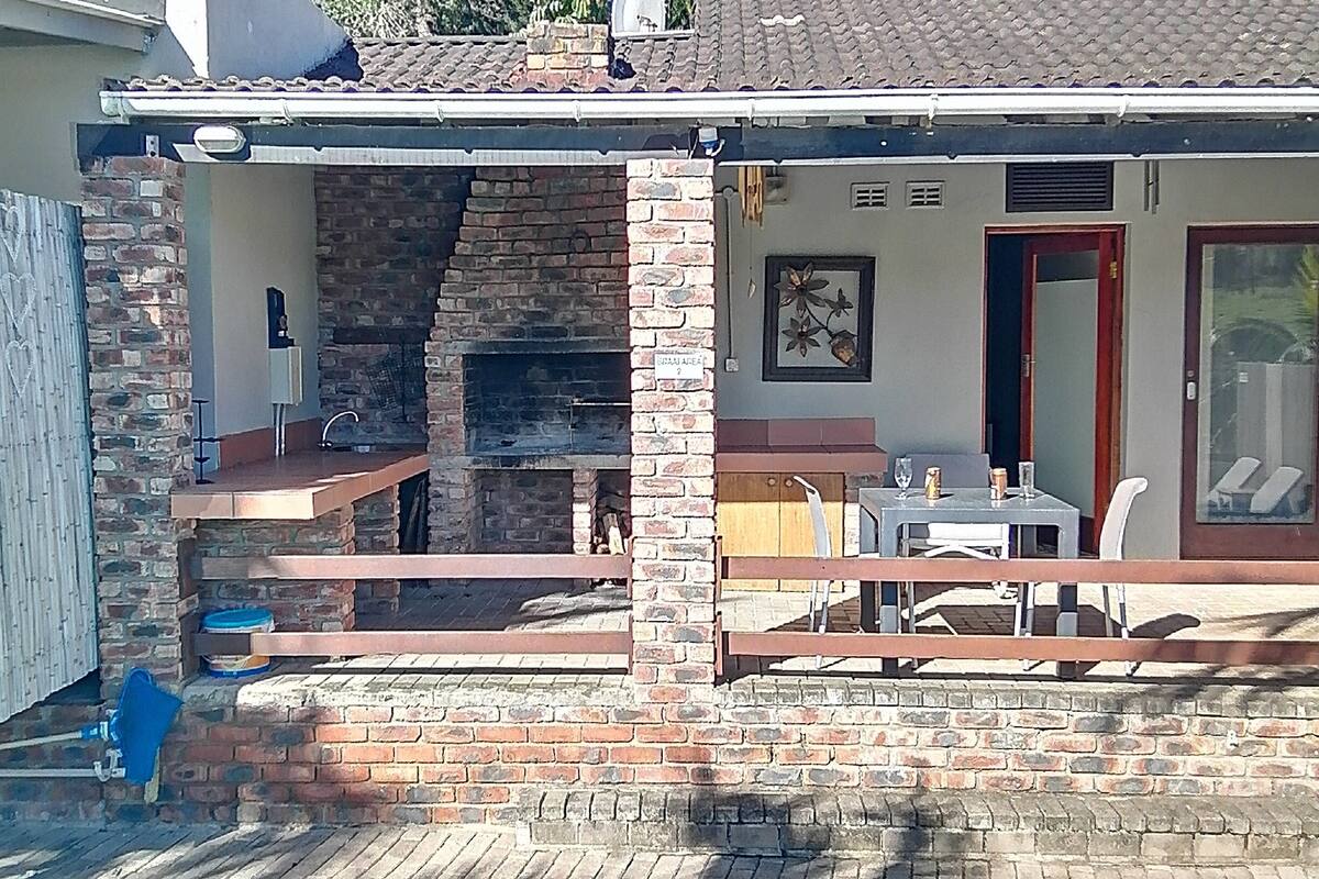 Un cortile con piscina, zona barbecue in mattoni e un'area pranzo.