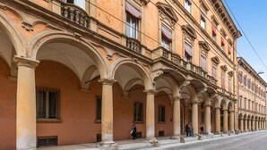 A historic building with a series of arches and columns, a cobblestone street, and a few people walking. - Primula Apartment by Wonderful Italy (Bologna)