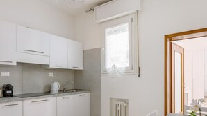 A modern kitchen with white cabinets, a built-in oven, and a window with blinds. - Primula Apartment by Wonderful Italy (Bologna)