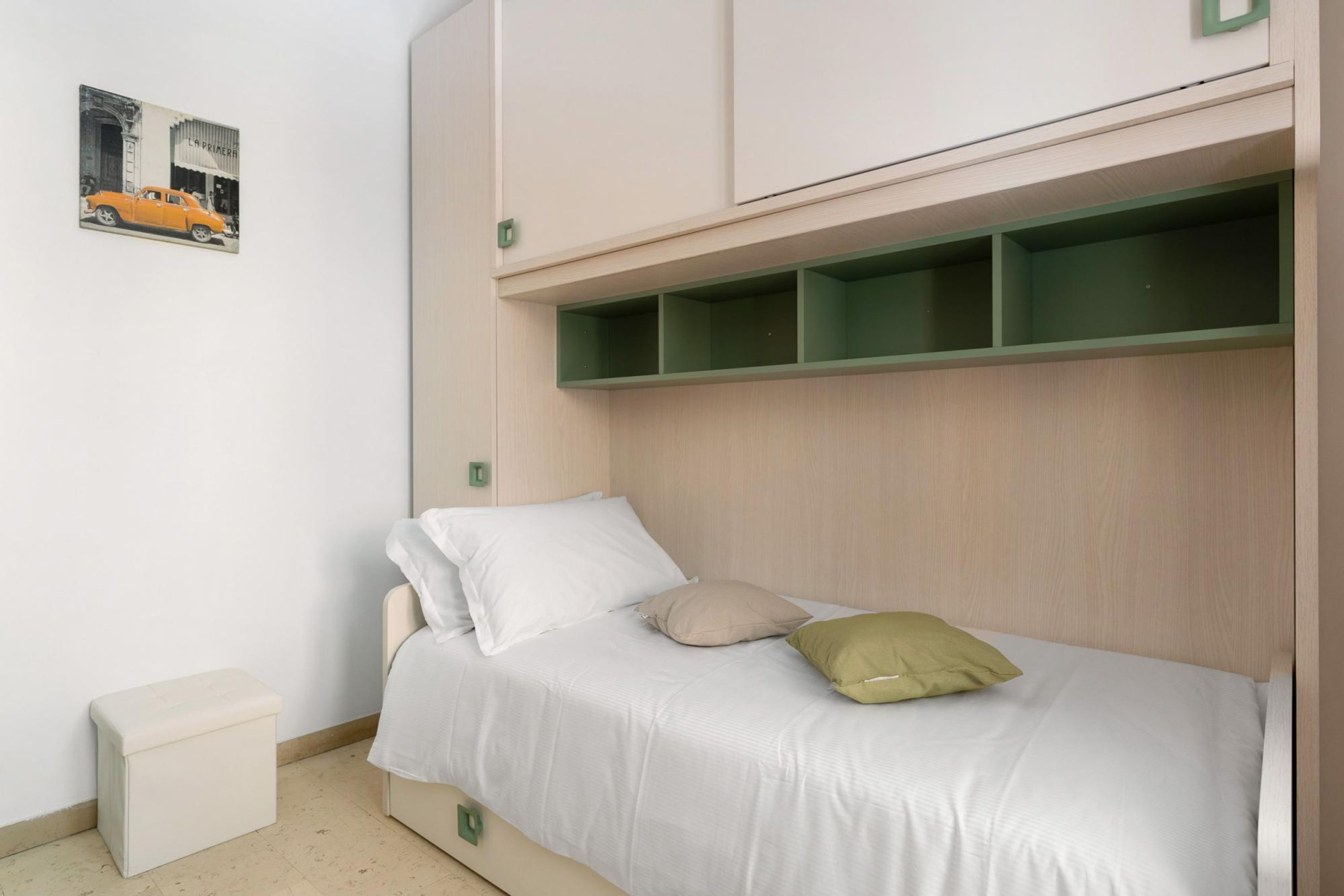 Een enkel bed met hoofdbord, een klein nachtkastje en een groene plank erboven.