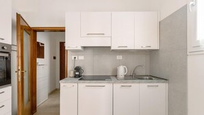 A modern kitchen with white cabinets, a stainless steel sink, and a coffee maker. - Primula Apartment by Wonderful Italy (Bologna)