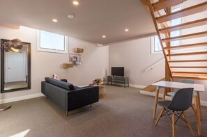 Relax in this stylish living room with a sofa, coffee table, dining table, and TV, surrounded by a high ceiling and a wooden staircase.