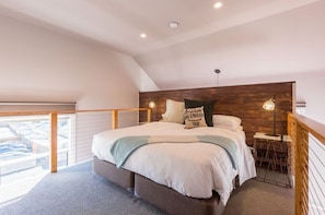 Relax in this serene bedroom with a large bed, wall-mounted light fixtures, and a balcony offering a view of the surrounding area.