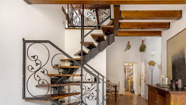 A staircase with a wrought iron railing, wooden beams, and a wall-mounted light fixture. - Country Style House in Bologna by Wonderful Italy (Bologna)