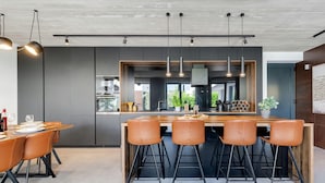 A modern kitchen with a central island, bar stools, pendant lighting, and a view of the city. - Villa Marli Zadarvillas (Nin)