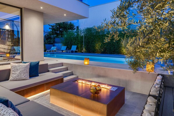 Un espacio al aire libre moderno con piscina, escalones de piedra y una chimenea.