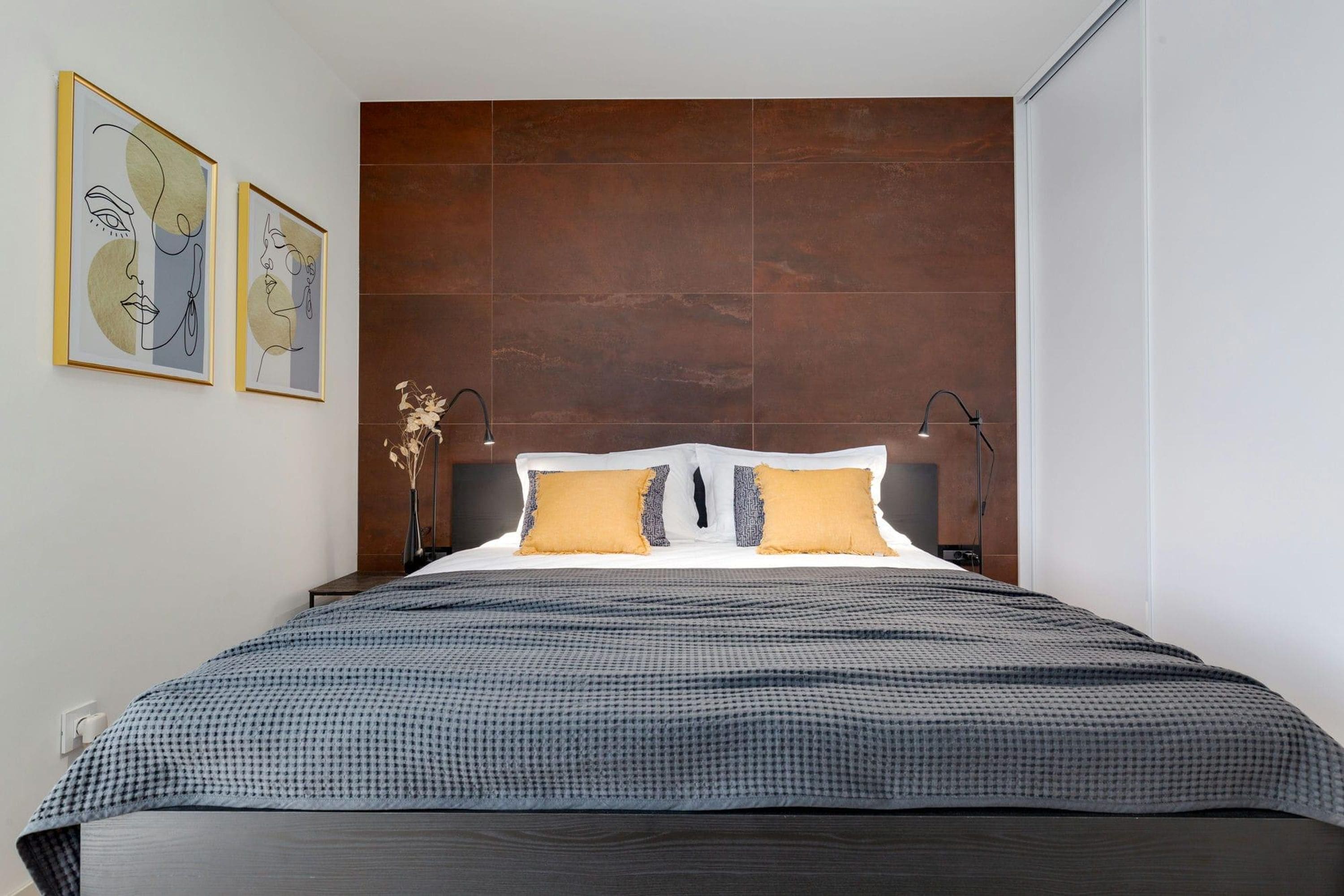 A modern bedroom with a large bed, two wall-mounted lamps, and abstract artwork on the wall.
